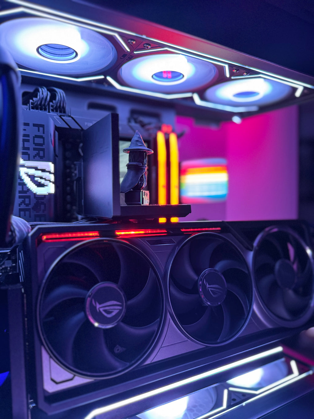 Close-up of a computer case with fans and RGB lighting, showing a colorful display in the background.