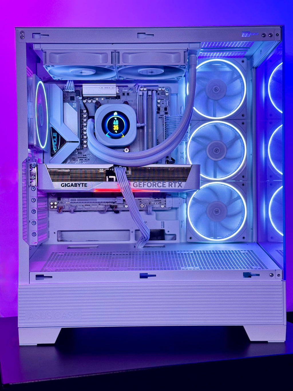 A white custom-built desktop PC with a liquid CPU cooler, a GIGABYTE GeForce RTX graphics card, and multiple illuminated blue and purple RGB fans inside a glass-sided case, set against a purple-lit background.