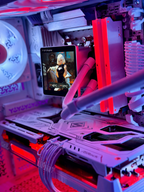 Close-up of a custom PC interior with white and light gray components illuminated by pink, purple, and red LED lighting. A small display screen is mounted on the front, showing a video, while cables and cooling tubes run through the chassis.
