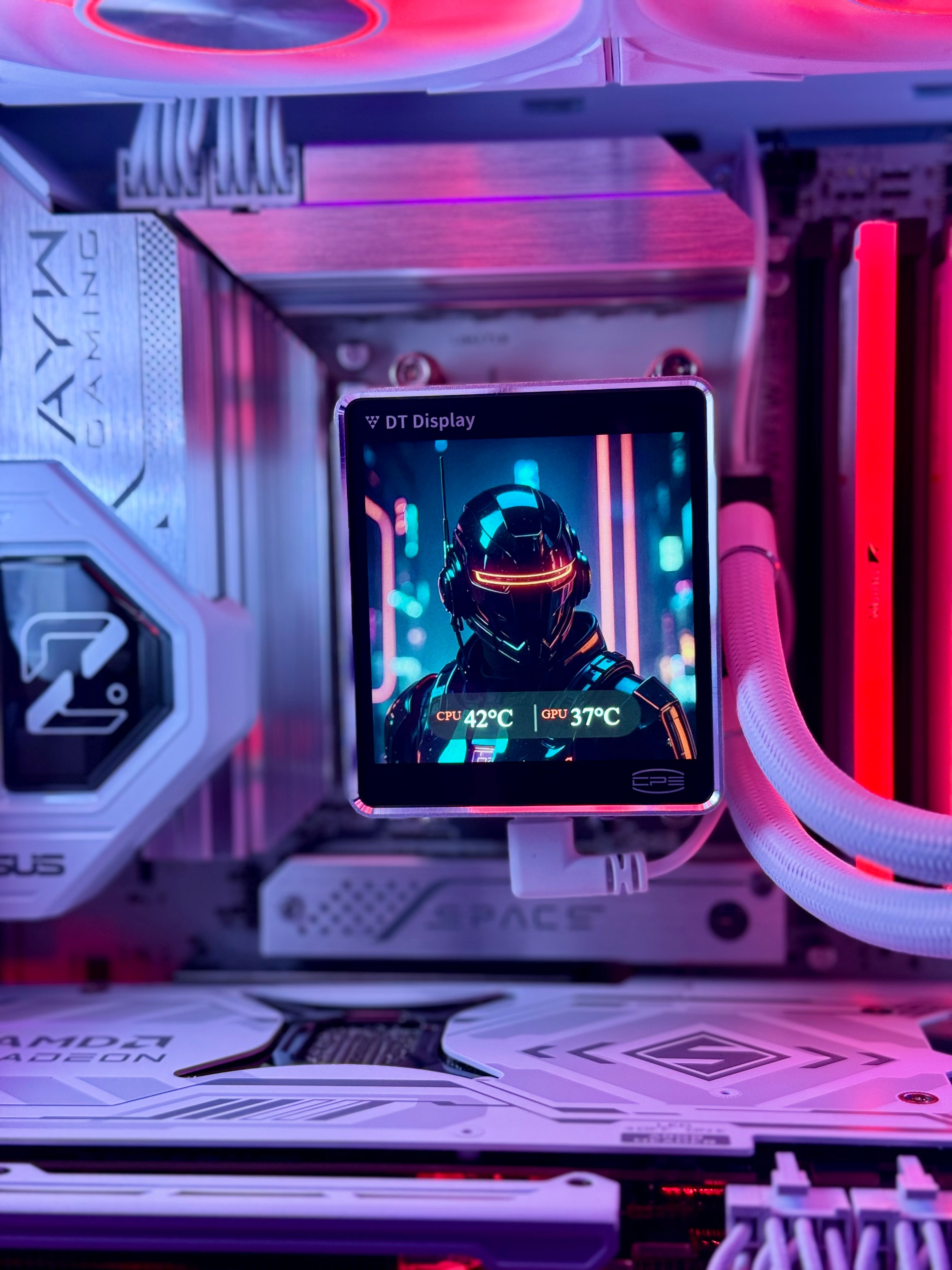 A desktop PC interior with RGB lighting in pink, purple, and red, featuring a small square in-circuit display screen mounted on the motherboard. The screen shows a futuristic helmeted character and temperature readings.