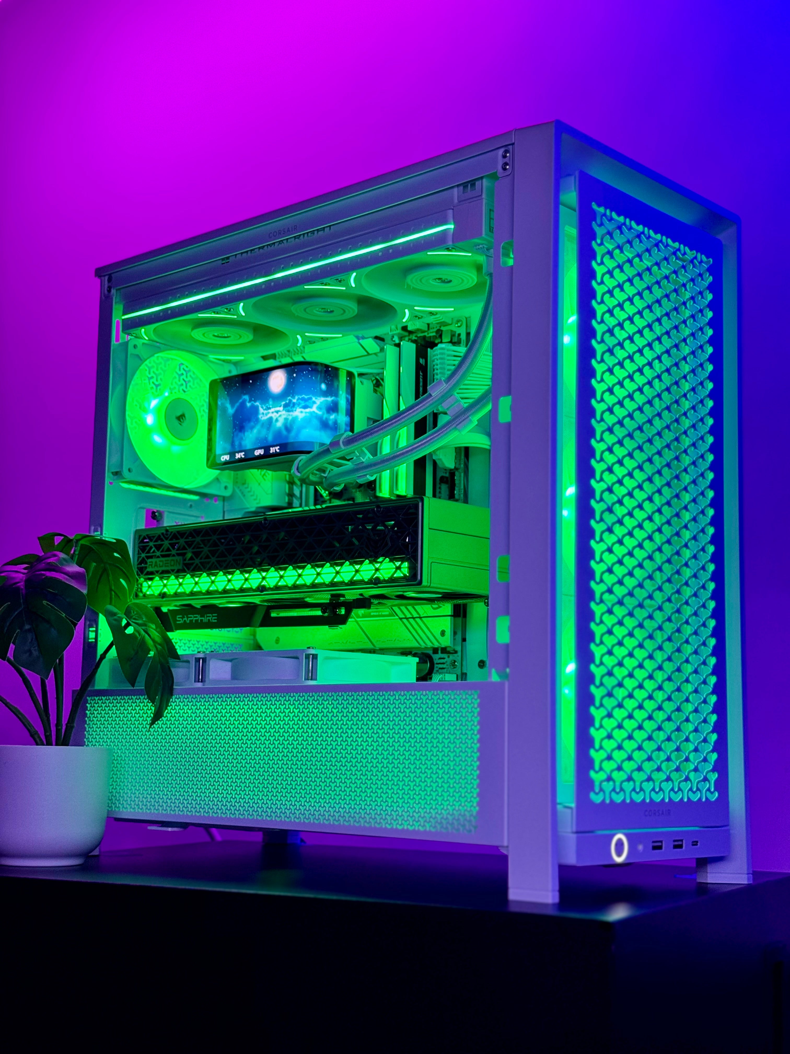 A custom white desktop PC tower with a clear side panel, showcasing a green-lit internal liquid CPU cooler with fans and tubing. The PC sits on a dark surface against a purple and pink ambient light background, with a potted plant on the left.
