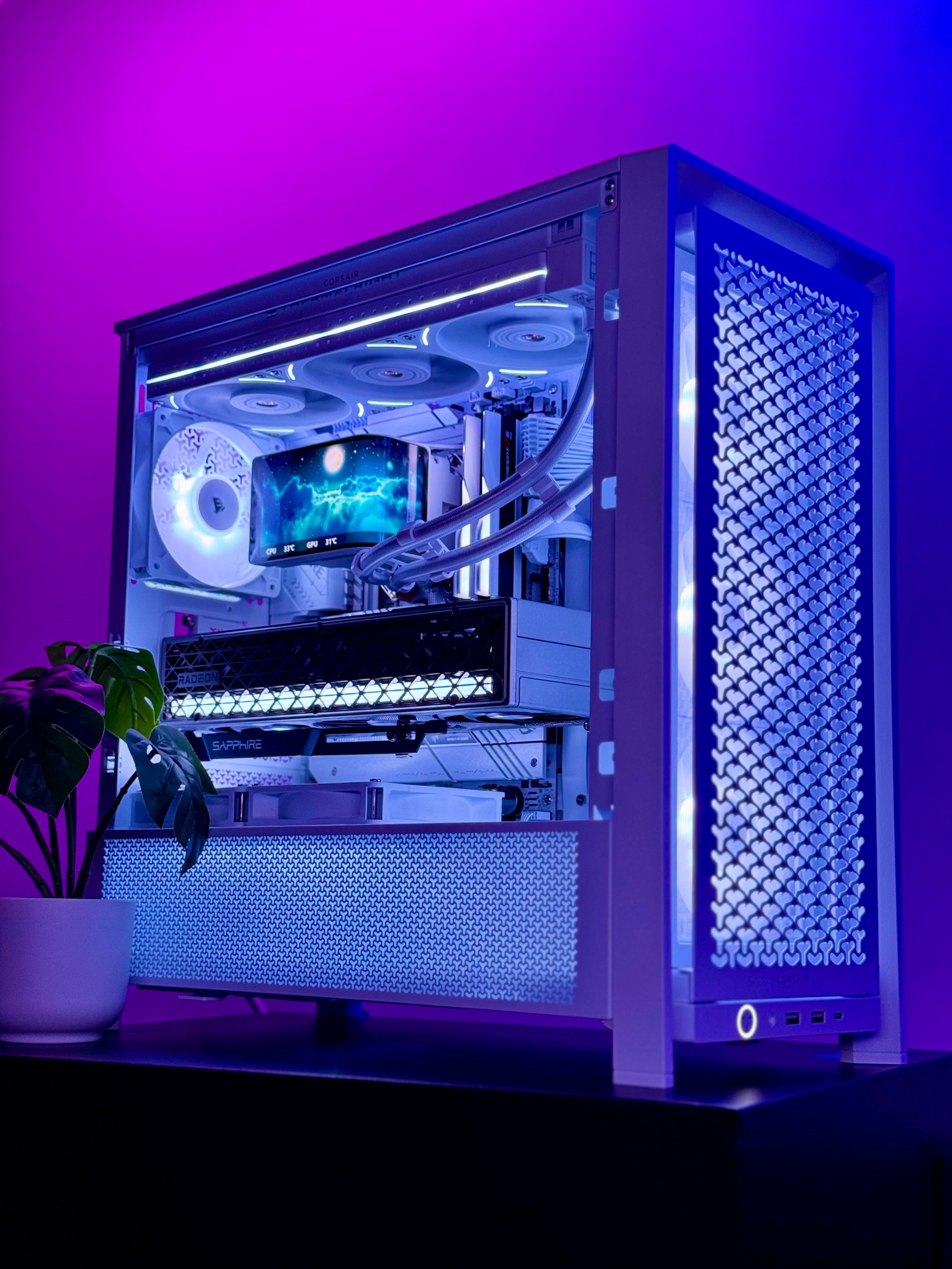 A custom-built desktop PC inside a white metal case with a glass side panel, showcasing a liquid CPU cooler, multiple cooling fans, and a graphics card. The setup is illuminated by cool blue and purple LED lighting, set against a matching purple-lit background with a small potted plant on the left.