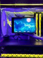 A close-up of a custom liquid CPU cooler with a transparent side panel, illuminated by purple and yellow LED lights. The cooler features a black radiator with a large purple fan, a tube carrying the coolant, and a digital temperature display screen showing CPU and GPU temperatures.