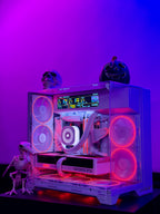 A custom white PC case with a transparent side panel, illuminated by pink and purple RGB fans and internal LED lighting. The case is decorated with Halloween props, including a skull, a jack-o'-lantern, and a small skeleton figurine, set against a purple and blue gradient background.