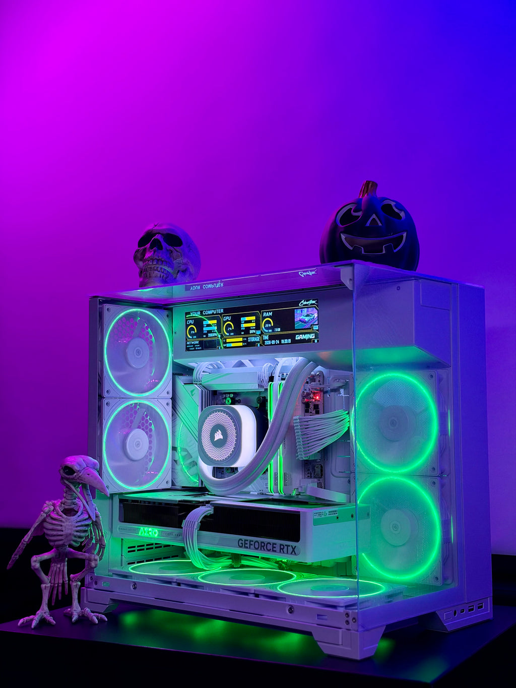 A custom white PC tower with glowing green and white RGB fans, a liquid cooler, and a GeForce RTX graphics card, styled with Halloween decorations including a skull, a pumpkin, and a small skeleton figurine against a purple and blue gradient background.