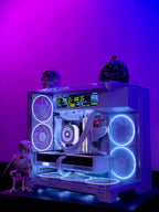 A custom white PC tower with a glass side panel, illuminated by blue and purple LED fans and internal lighting. The PC is styled with Halloween decorations, including a skull, a jack-o'-lantern, and a small skeleton figurine, set against a vibrant purple and blue gradient background.