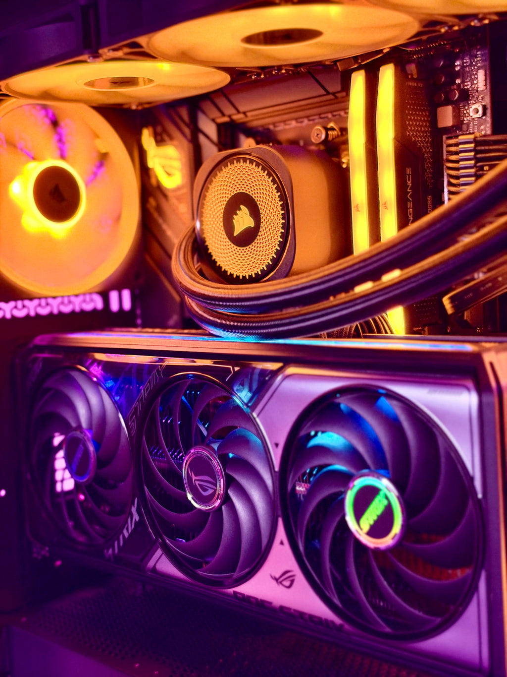 Close-up of a high-performance PC interior with a triple-fan graphics card in the foreground, illuminated by purple and blue LED lighting, alongside a CPU cooler and yellow-lit fans in the background.